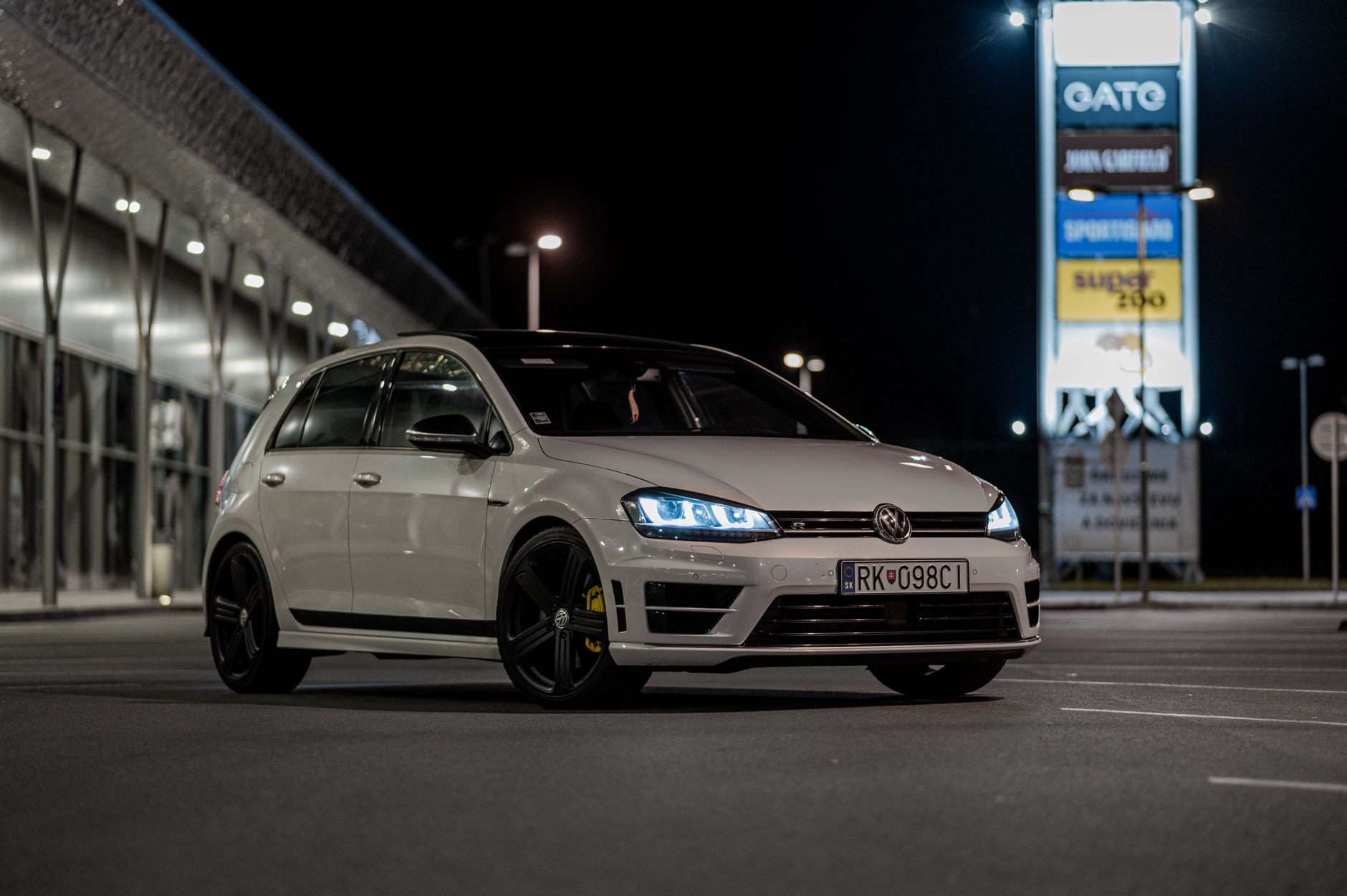 White Volkswagen sports car parked under streetlights in Liptovský Mikuláš, Slovakia at night.