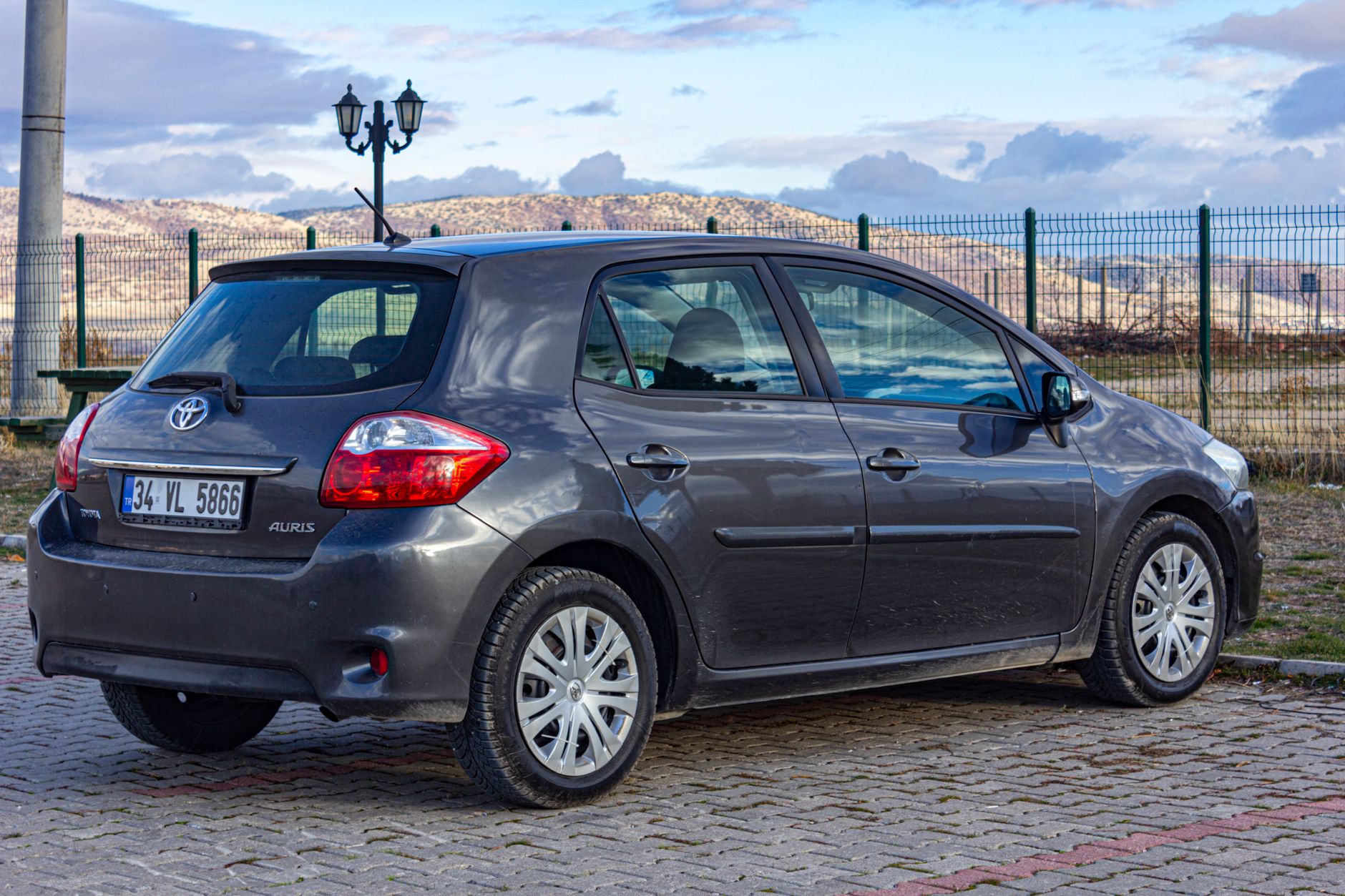 A gray Toyota Auris parked outdoors with hills and cloudy sky in the background.