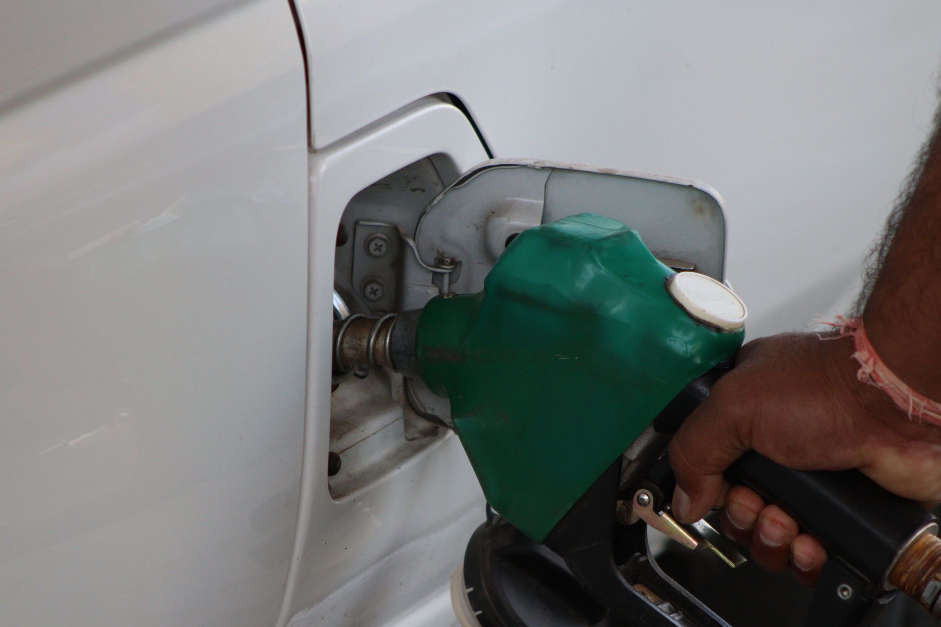 Close-up of a hand refilling a car's gas tank at a station with a green fuel nozzle.