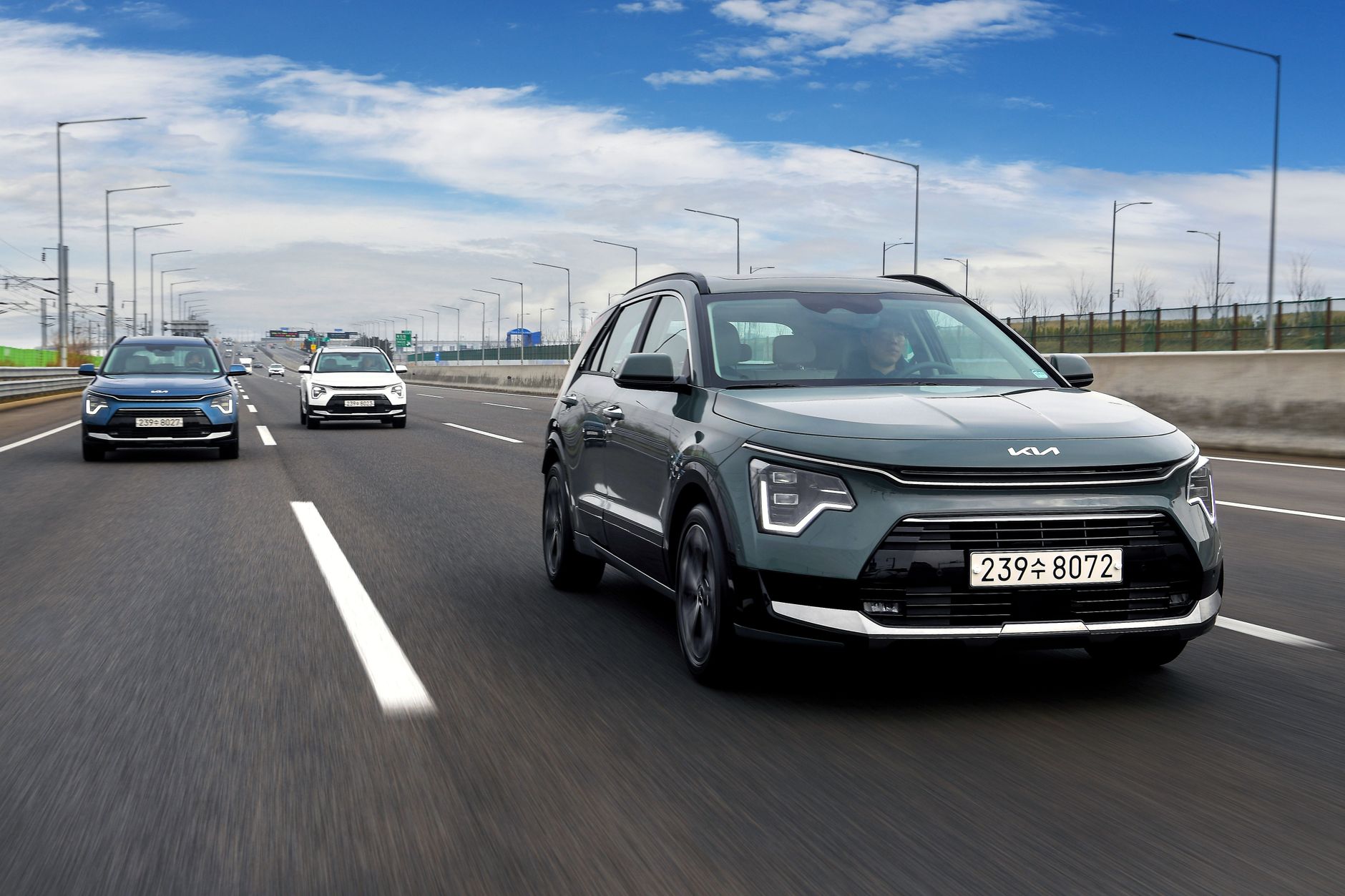 Kia Niro SUVs driving on a highway under a bright blue sky, showcasing speed and modern design.