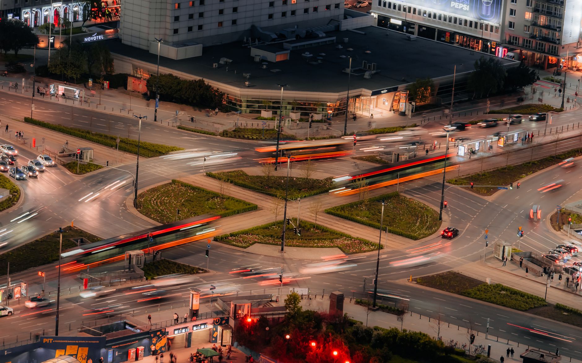 A dynamic aerial view of a busy intersection at night with blurred traffic lights and cityscape.