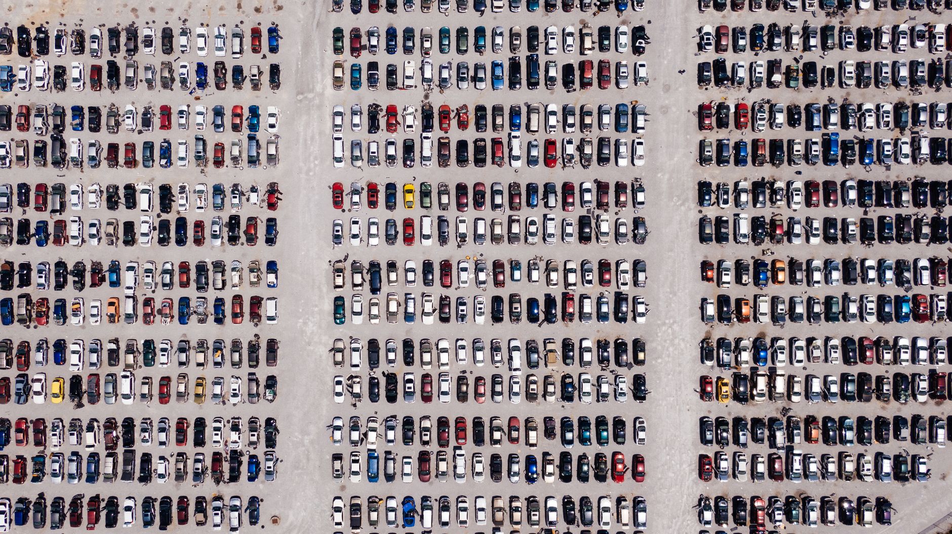 A high-angle aerial shot showing rows of parked cars in a large outdoor parking lot.