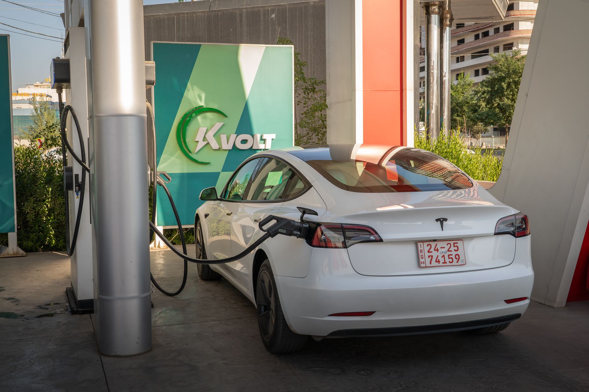 A white Tesla Model 3 charging at an outdoor electric vehicle station with Kvolt branding.