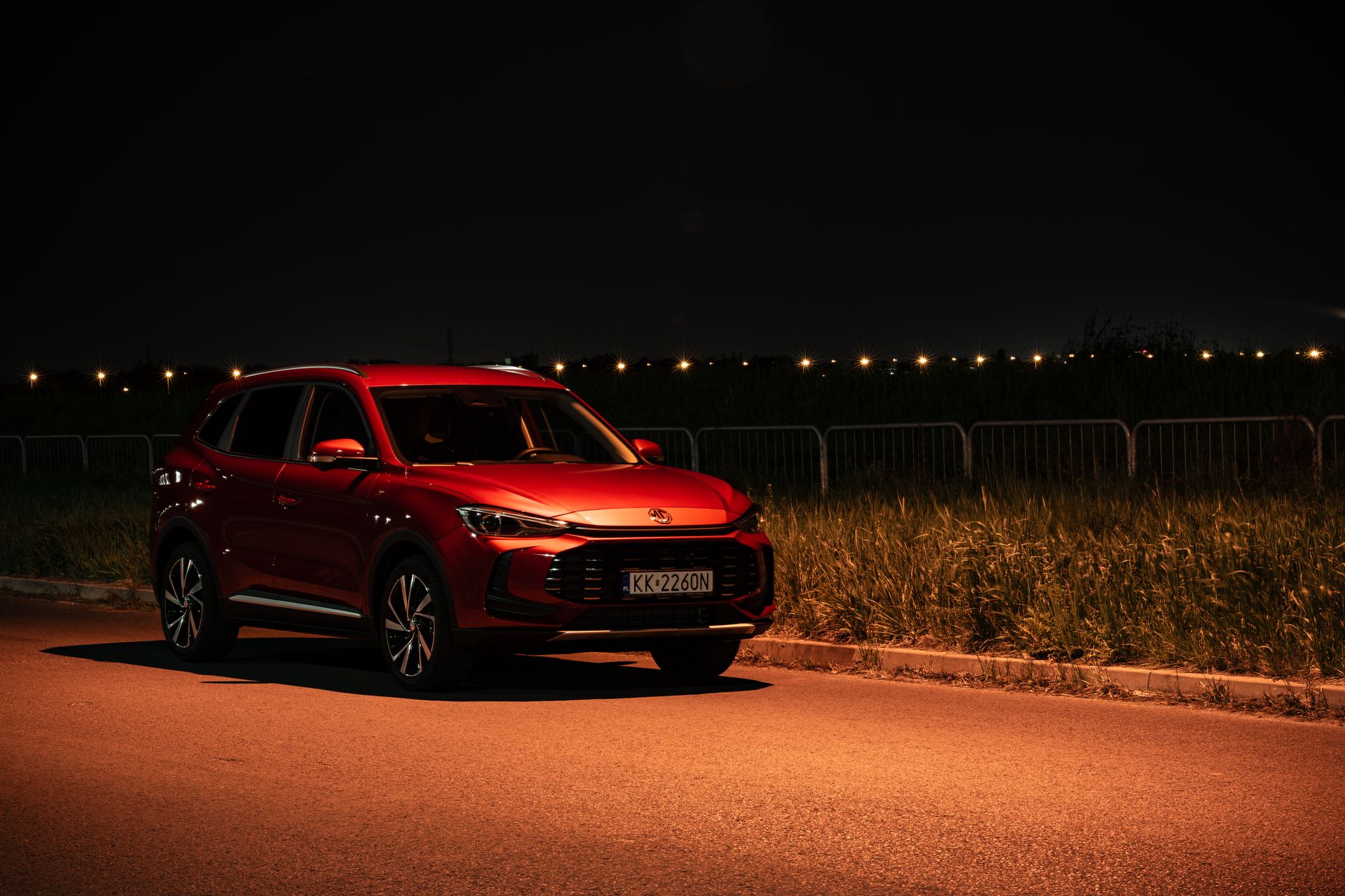 Red SUV parked on a street at night in Kokotów, Poland, with warm streetlights creating a dramatic effect.