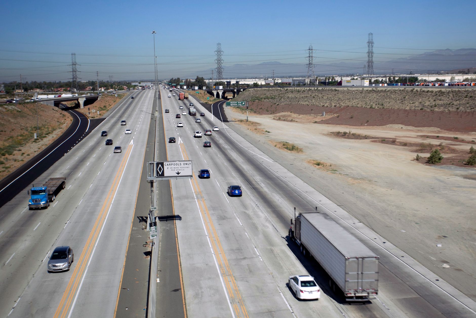 Wide aerial view of a highway with vehicles under a bright blue sky.