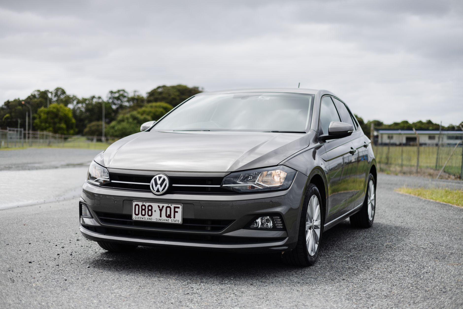 A silver Volkswagen Polo parked in a rural area with overcast skies, showcasing its design.