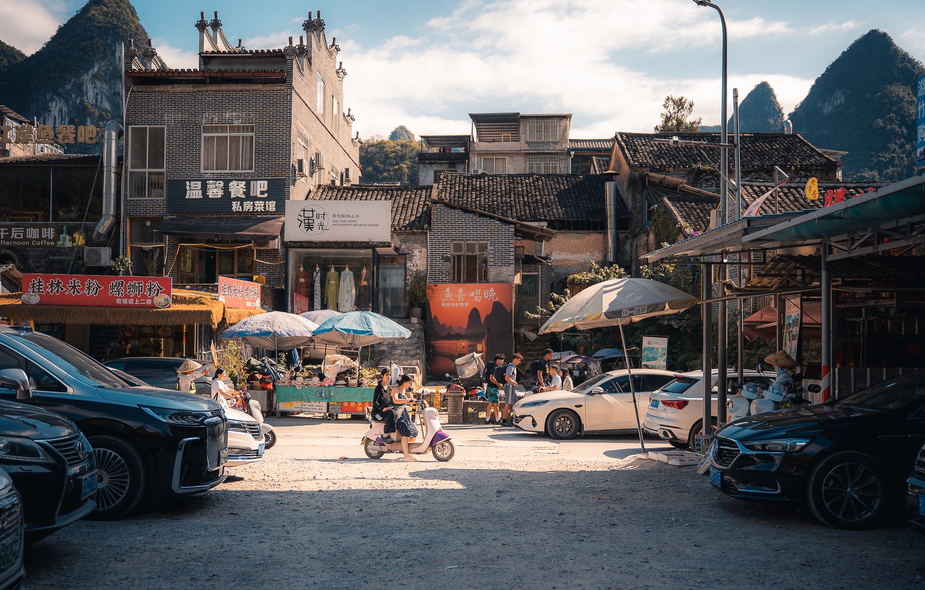 Vibrant street scene in Xingping, China featuring parked cars, motorcycles, and local shops under a sunny sky.