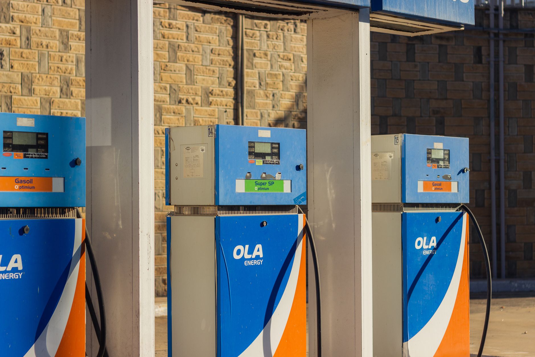Three blue OLA Energy gas pumps at an outdoor station on a sunny day.