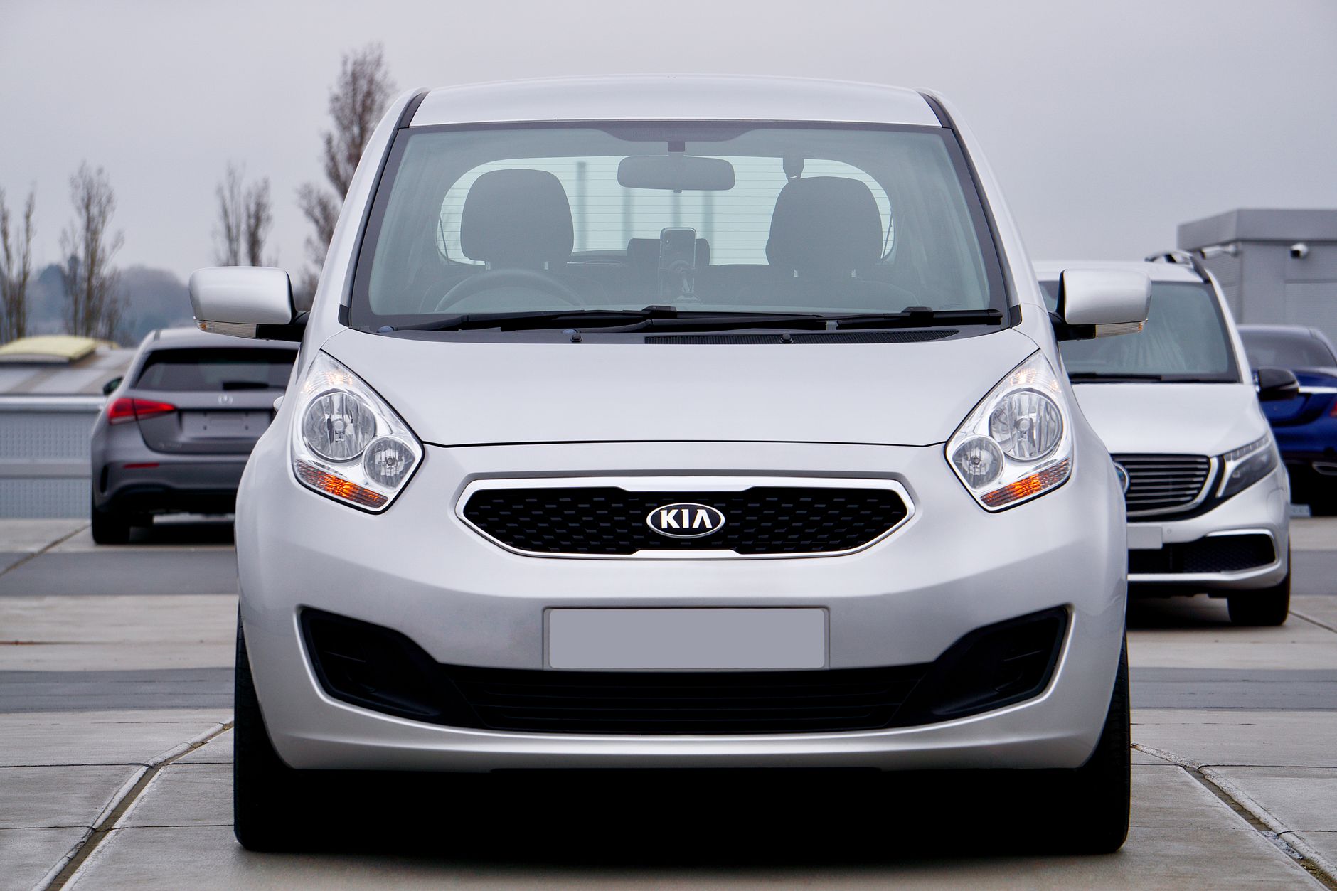 A silver Kia car is parked in a parking lot, captured from the front view.