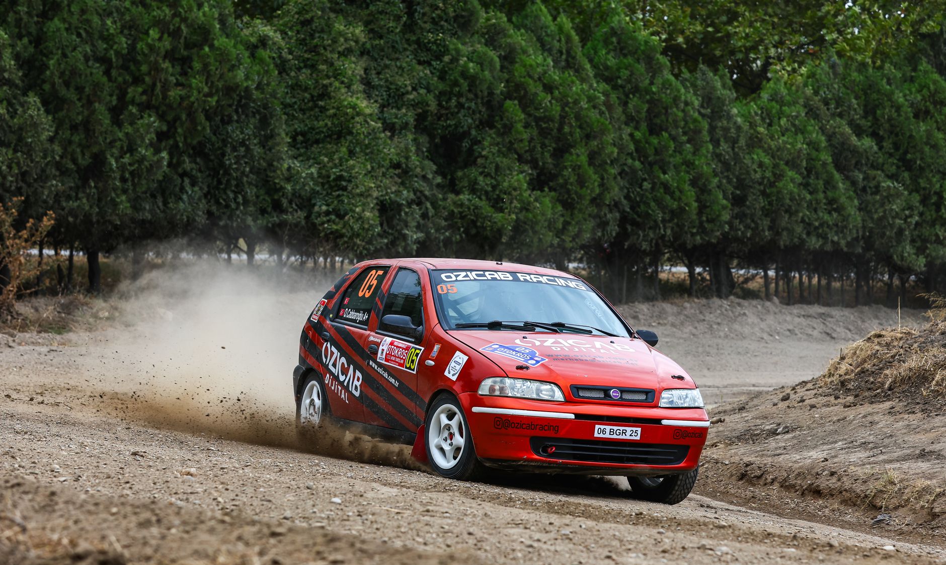 Fiat racing car in action on a dirt track during a rally event with dust trail.