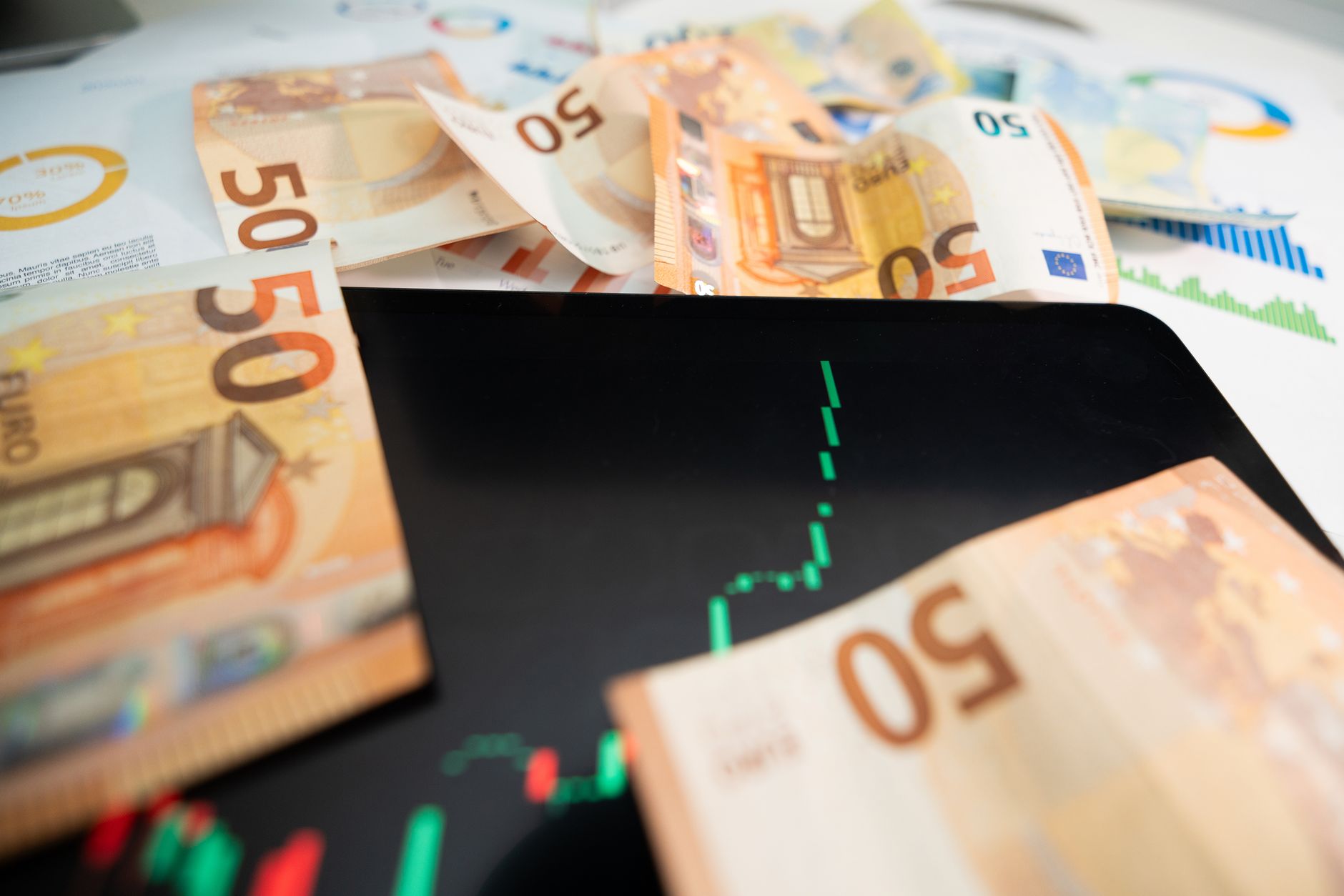 Close-up of 50 euro banknotes with a digital stock market chart on a tablet, depicting financial growth.