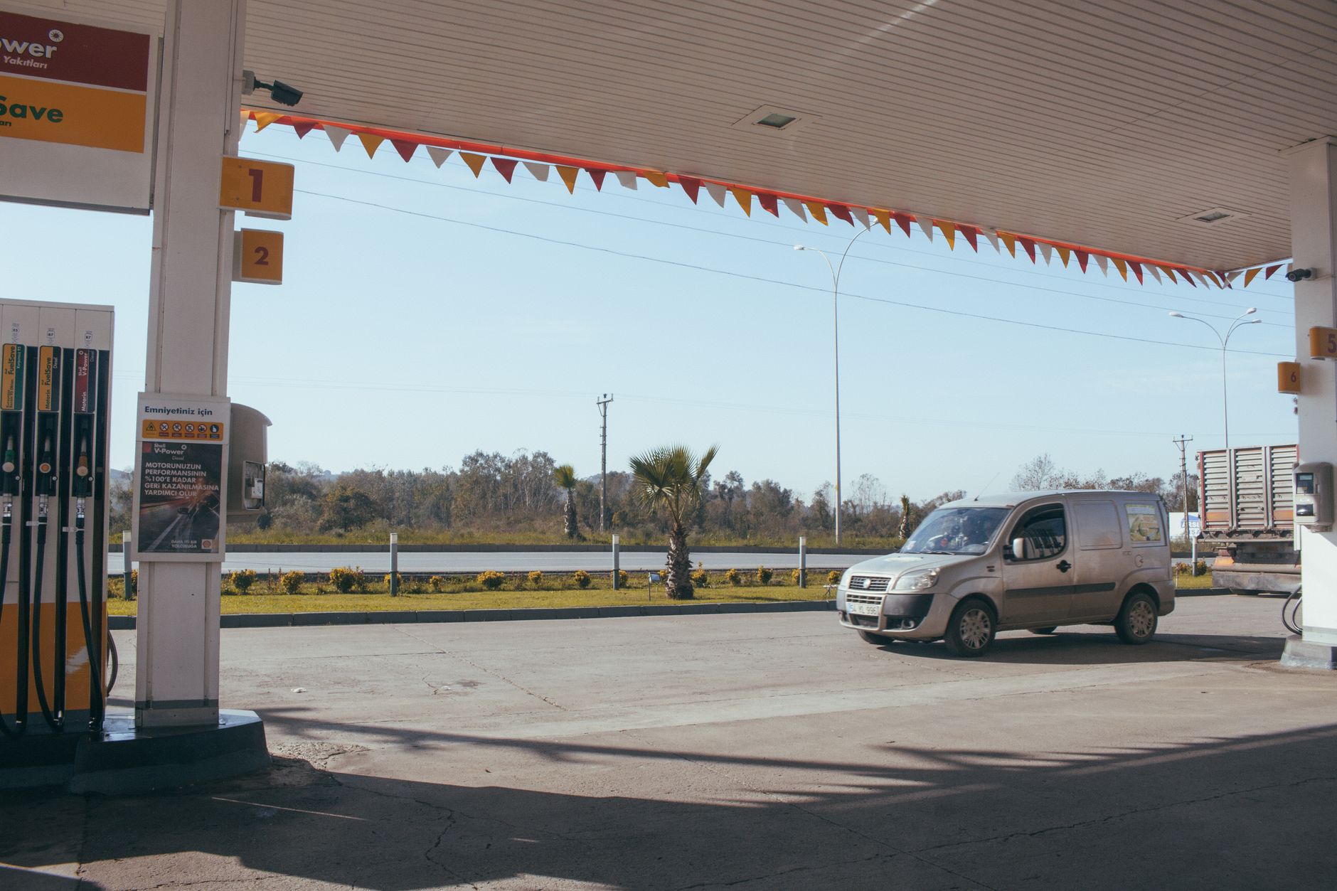 Van car driving along asphalt road near gas station in suburb on sunny day