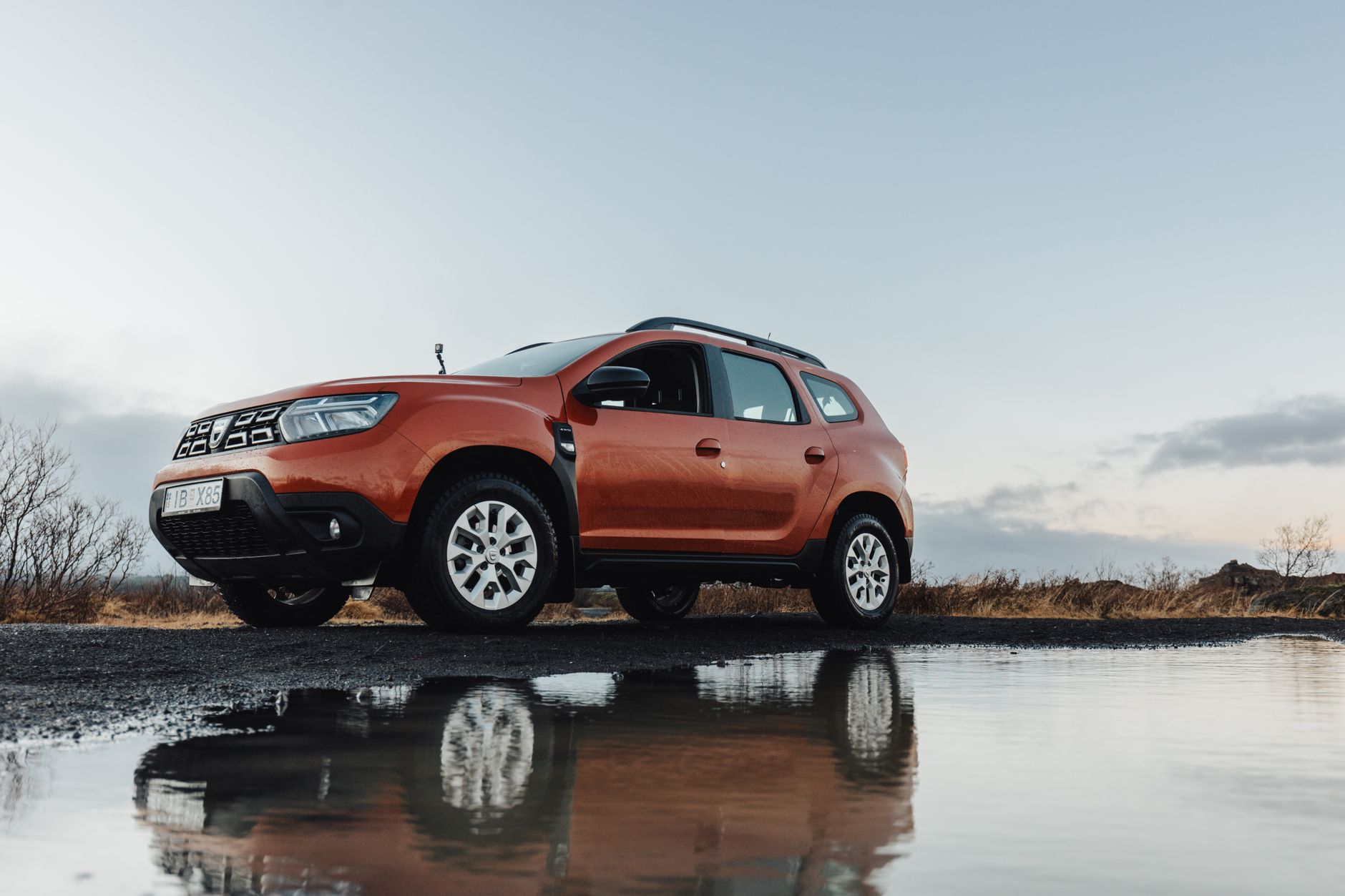A rugged orange SUV reflected in a puddle on a rural road, showcasing adventure and exploration.
