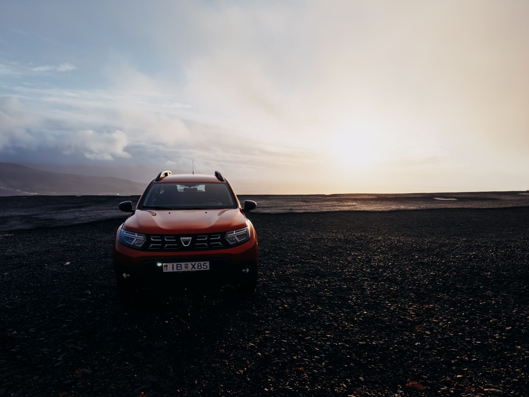 A red SUV parked on a rocky landscape under a dramatic sunrise, showcasing offroad capability.